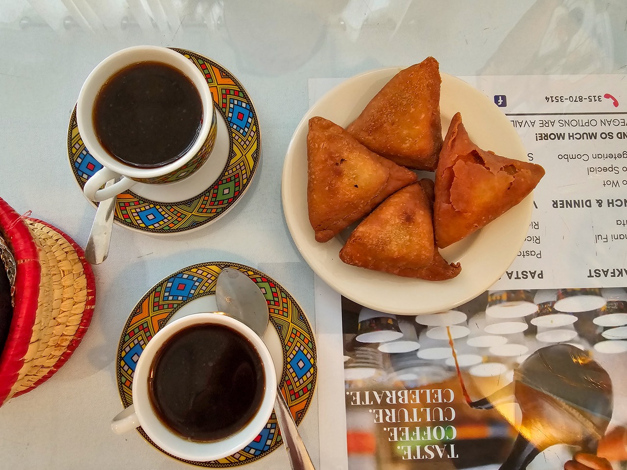 An overhead photo of two cups of black Ethiopian coffee, along with a plate of fried sambusa.