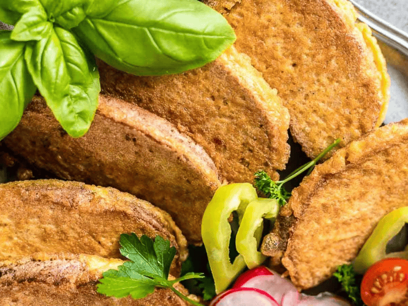 Several crispy tacos are arranged together, garnished with fresh basil, sliced radishes, green peppers, and parsley.