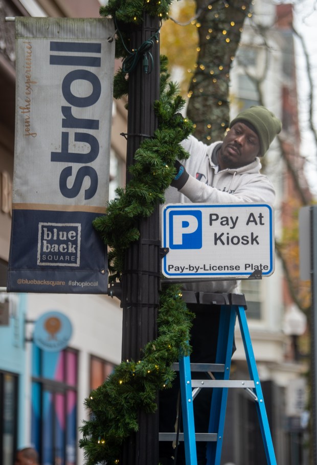 Shawn Fogle, of Atria, uses a zip tie to secure garland to a light post at Blue Back Square in West Hartford on Wednesday, Nov. 5, 2025. Crew members from Atria will be preparing the area for the holidays over the next few days. (Aaron Flaum/Hartford Courant)