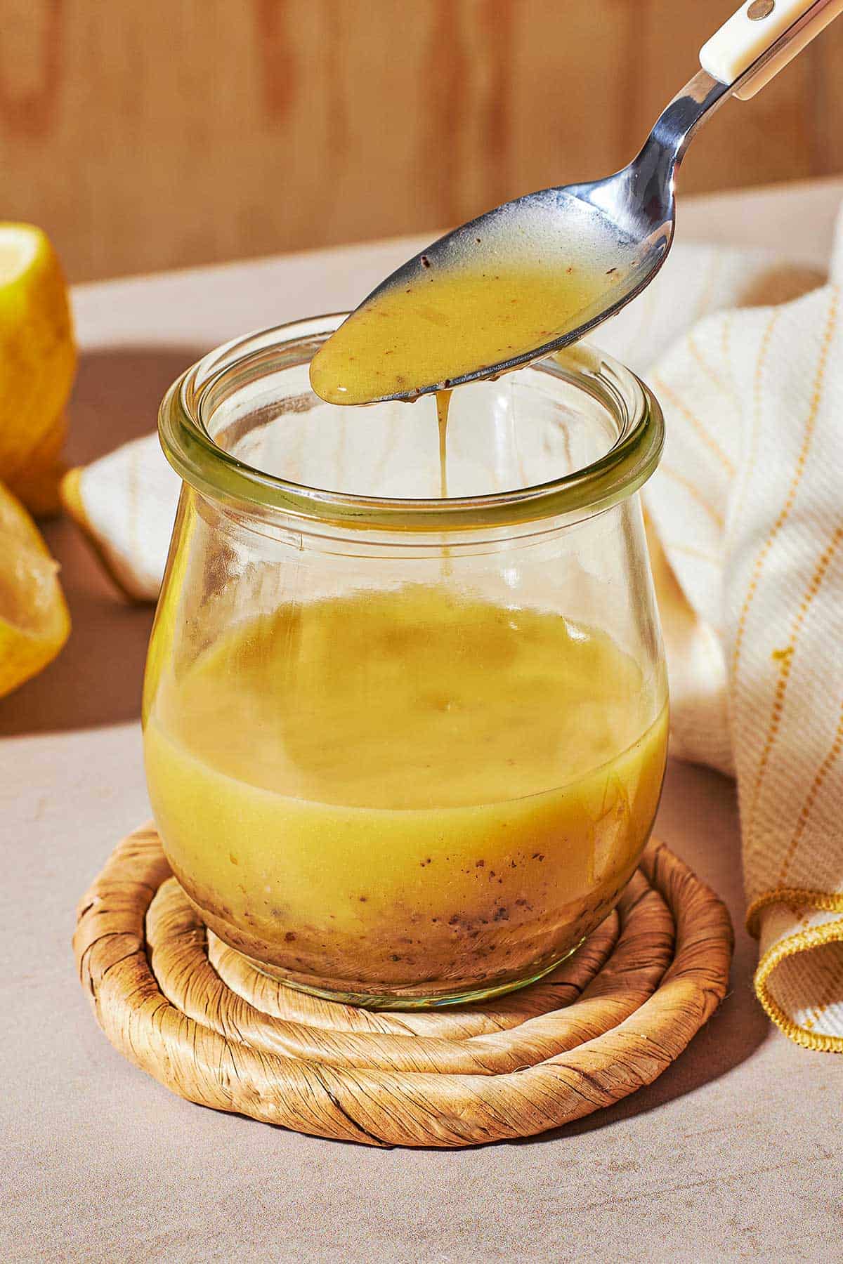 a close up of dijon vinaigrette in a glass jar, with a bit being lifted out with a spoon.