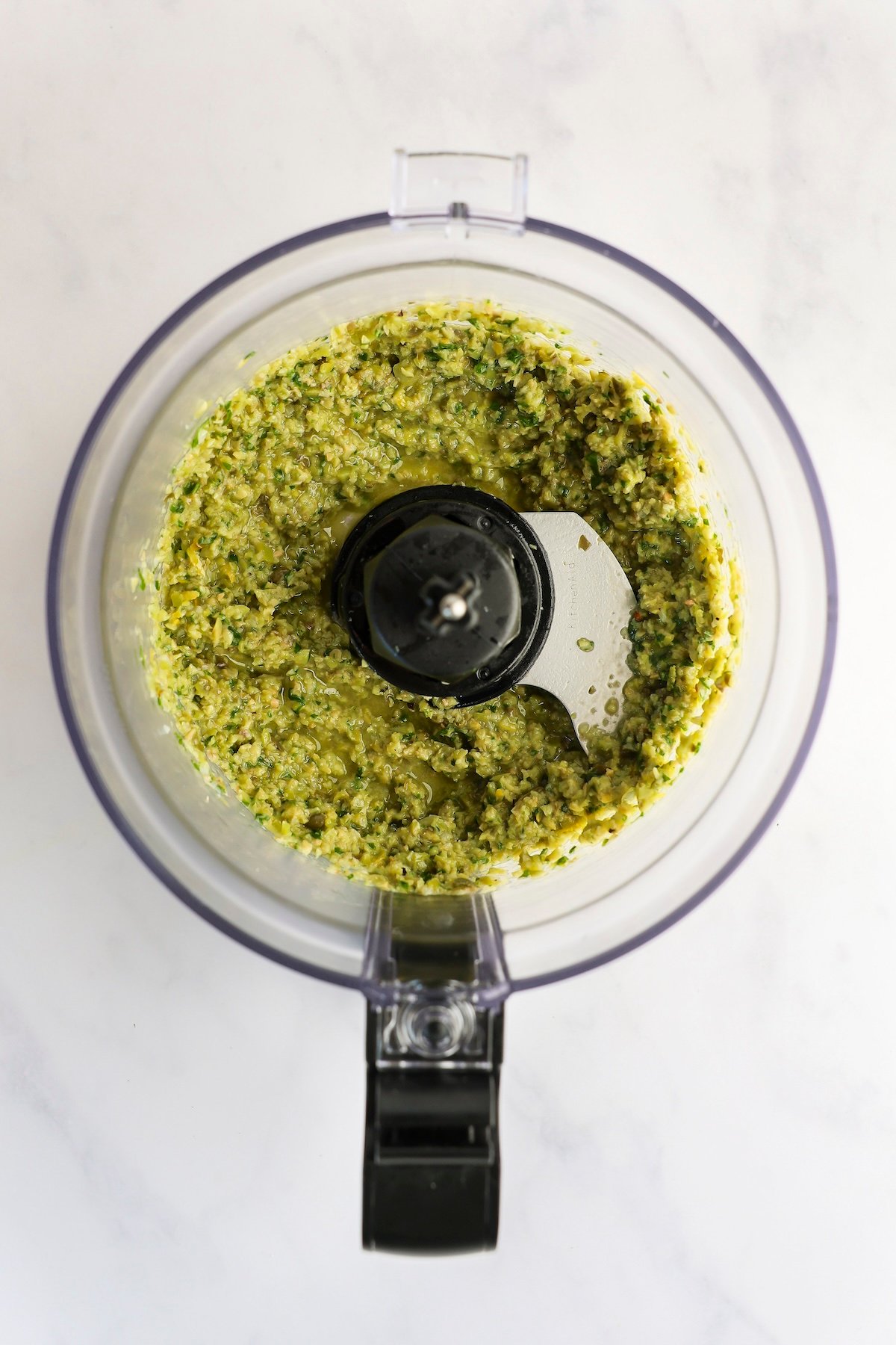 food processor with olive oil combined with minced garlic, basil, olives, capers, anchovy paste, lemon zest, lemon juice, and pepper