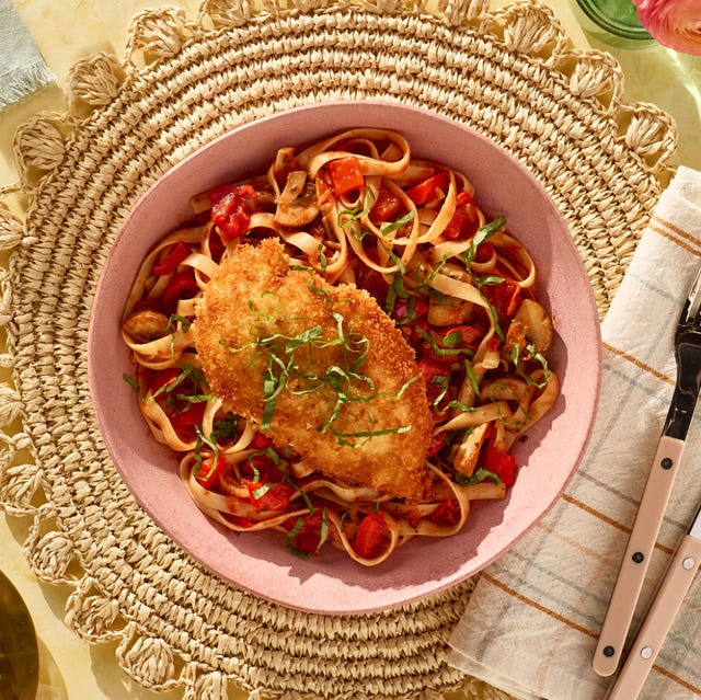 A plate of pasta with a crispy chicken cutlet on top, garnished with basil herbs.