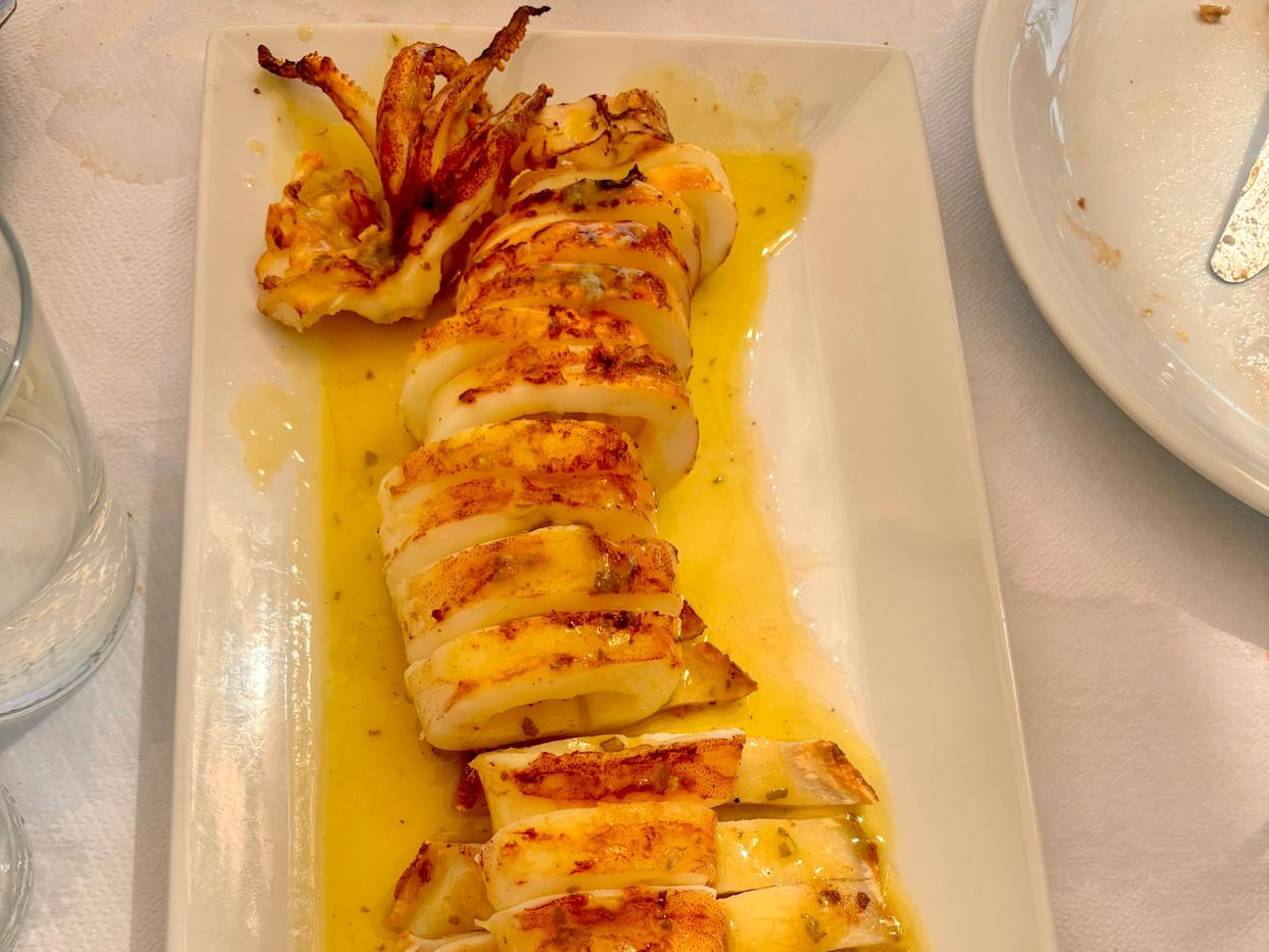 A plate o grilled calamari in a thin yellow sauce.