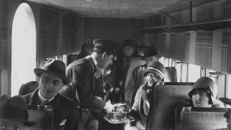 a black and white photo featuring a waiter serving champage on a plane