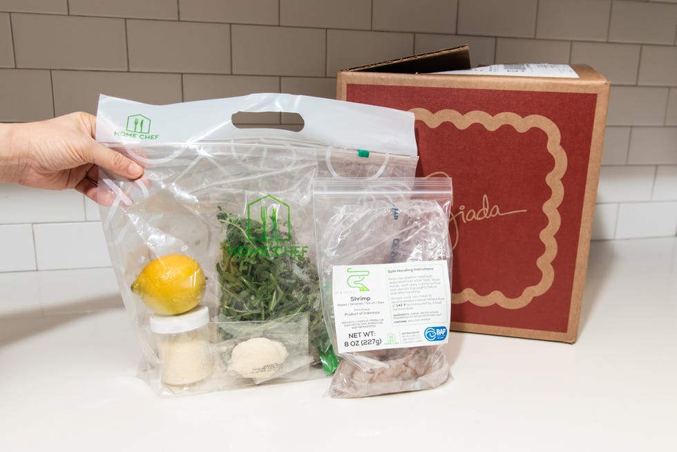 bags filled with lemon, arugula, shrimp and other ingredients from meal kit in front of red box