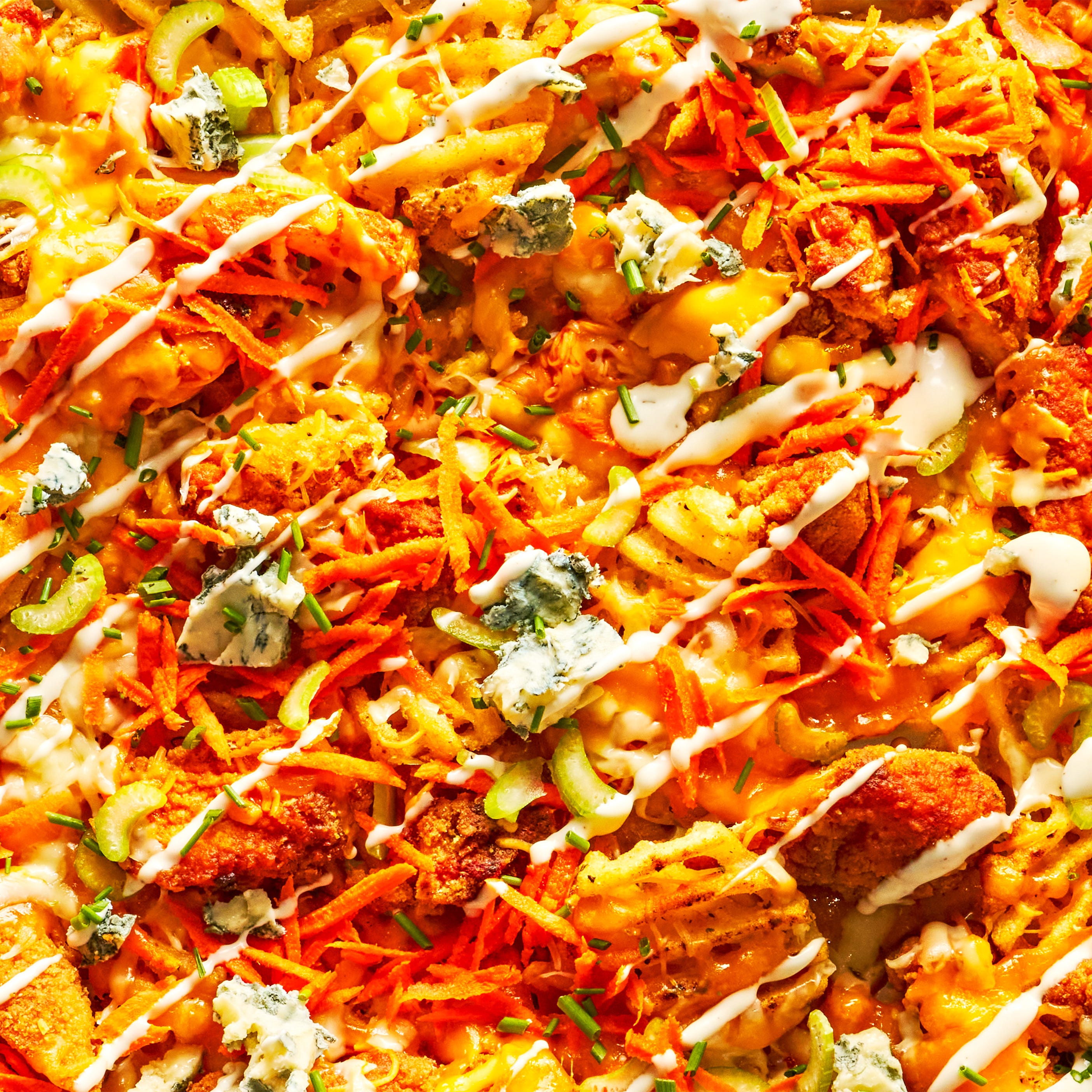 waffle fries on a sheet pan topped with buffalo chicken, carrots, celery, and blue cheese