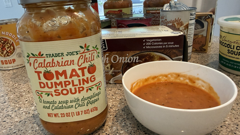 Trader Joe's Calabrian Chili Tomato Dumpling Soup next to some in a white bowl with other TJ's soups in background