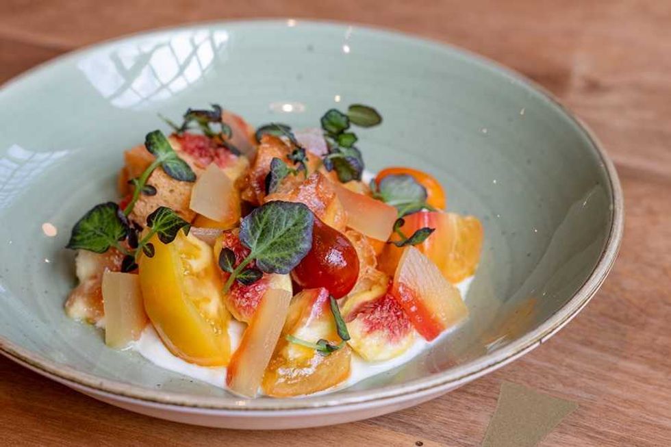 Colorful heirloom tomato salad with figs and greens on a light blue plate.