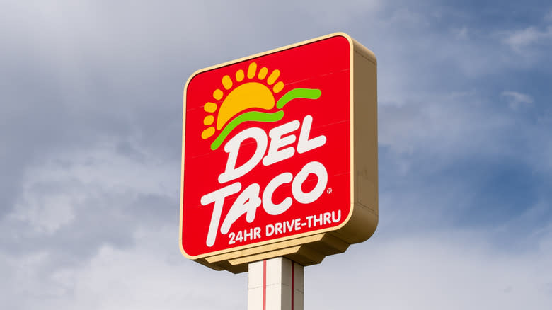 A Del Taco sign is seen against a slightly cloudy sky