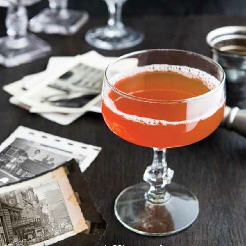 cocktail glass with a reddish drink surrounded by vintage photographs