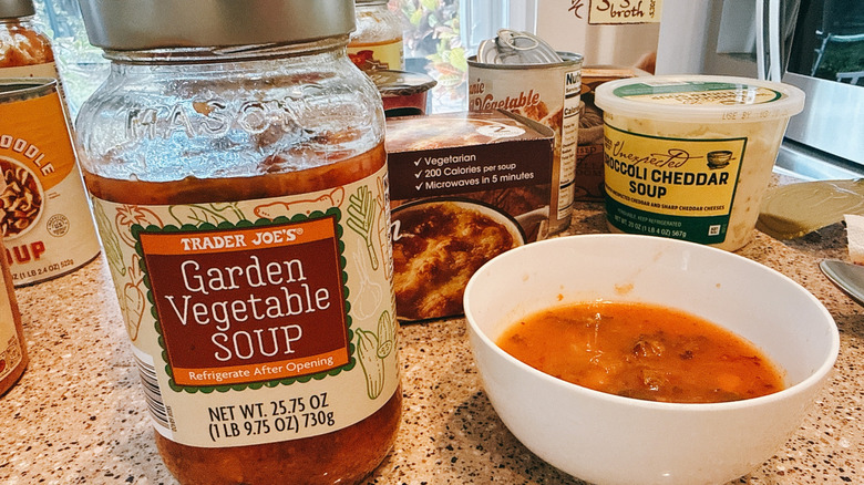 Jar of Trader Joe's Garden Vegetable Soup next to some in a white bowl with other TJ's soups in background