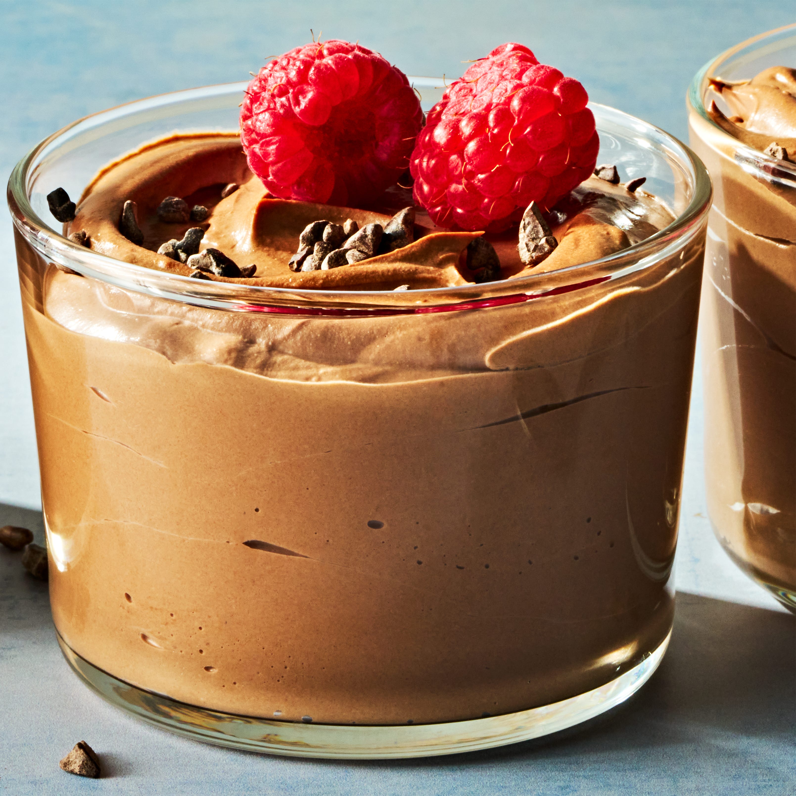 chocolate mousse in a cup topped with chocolate pieces and raspberries