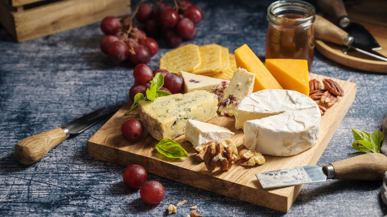 cheeses on a wooden cutting board with grapes and nuts