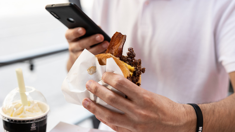 person on phone with burger and milkshake