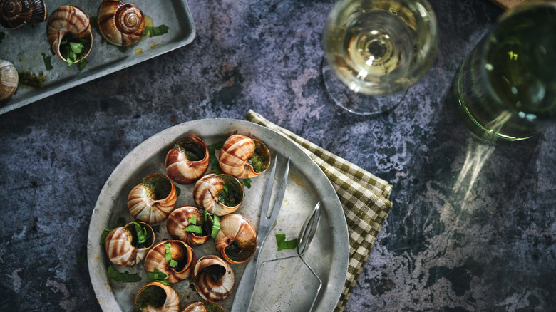 Tray and plate with escargot on marble table with white wine