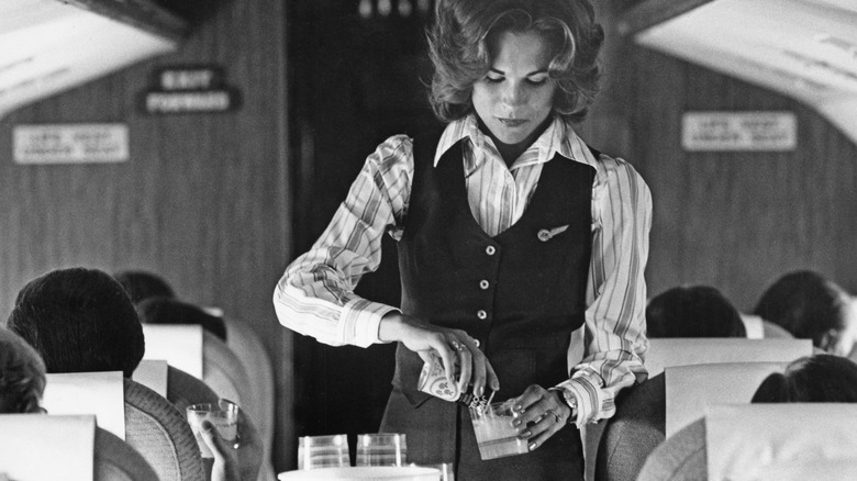 a black and white photo with a flight attendant pouring a beverage
