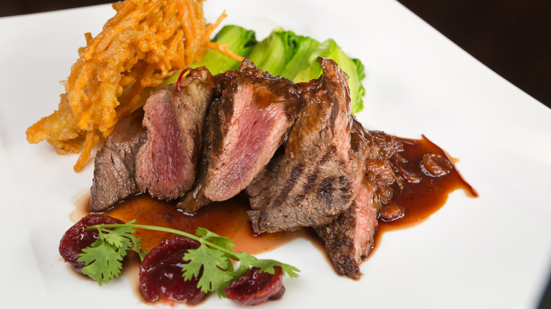 Rare-cooked kangaroo steak on a plate with jus, vegetables, and garnishes