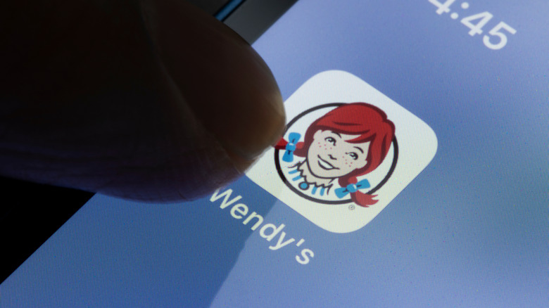 Person touching the Wendy's app icon on a smartphone screen