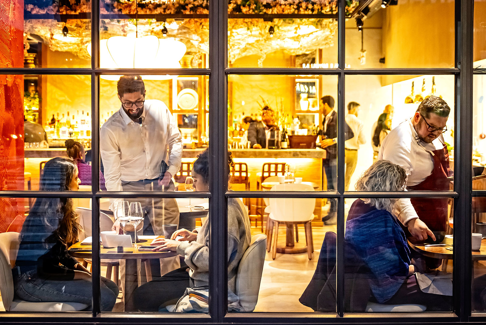 View of diners inside warmly-lit restaurant through window panes