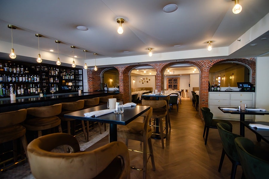 Interior of a fine-dining restaurant, featuring a stately bar area, exposed brick archways, and a well-lit dining room with white tablecloths.