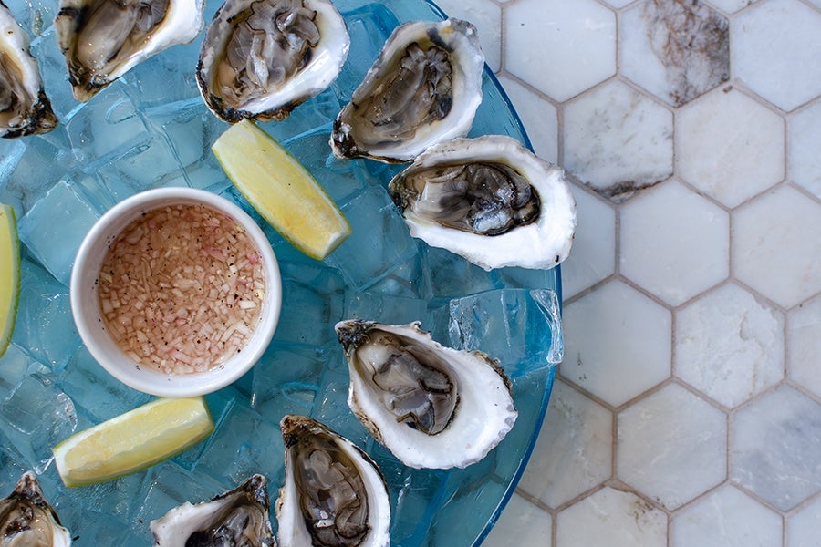 Overhead view of a transparent blue platter of oysters on the half shell with lemon wedges and mignonette.