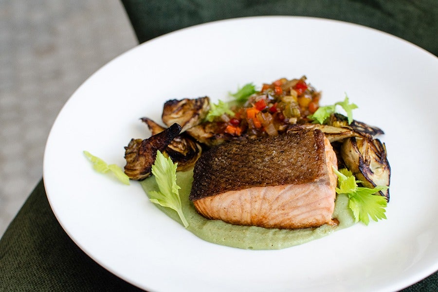 Salmon with seared skin sits on a green puree next to charred artichokes.