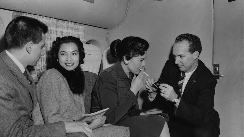 a man lights a woman's cigarette on an airplane