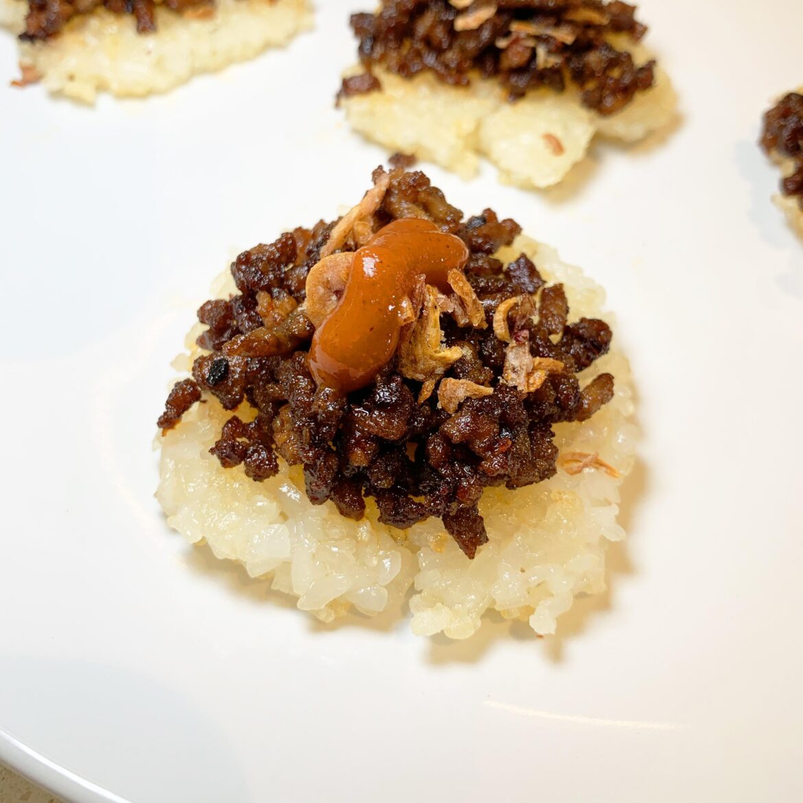 Sweet Soy Beef & Onion on Crispy Flat Rice 🔥 Topped with Fried Shallots & Sriracha