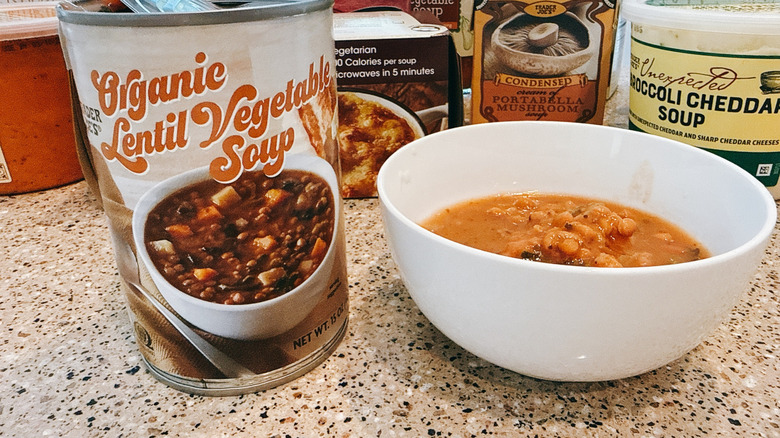 Can of Trader Joe's Lentil Vegetable soup next to some in a white bowl with other TJ's soups in background