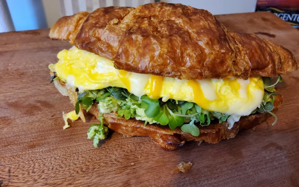 Egg croissant with cheddar on bed of microgreens and avocado.