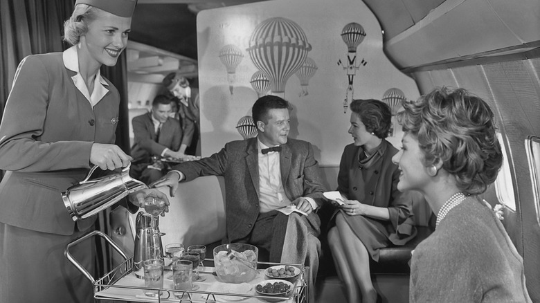a black and white phot with a flight attendant serving a passenger a drink