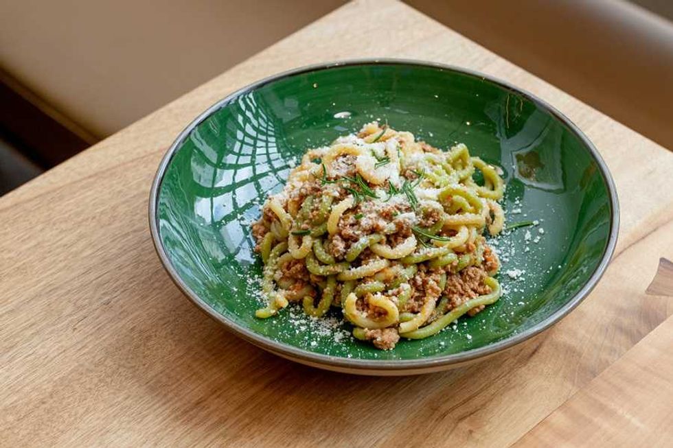 Pasta with meat sauce and cheese in a green bowl on a wooden table.
