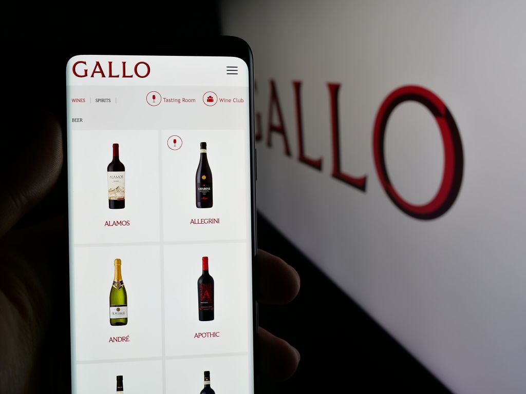 Illustration of a person holding a cellphone displaying the E. J. Gallo Winery webpage with wine bottle images.
