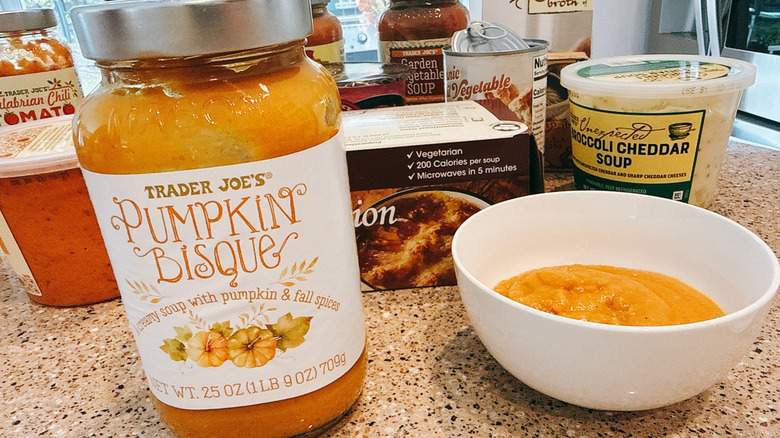 Jar of Trader Joe's Pumpkin Bisque Soup next to some in a white bowl with other TJ's soups in background
