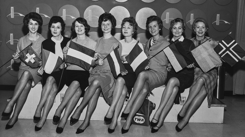 eight TWA flight attendants hold country flags while sitting down