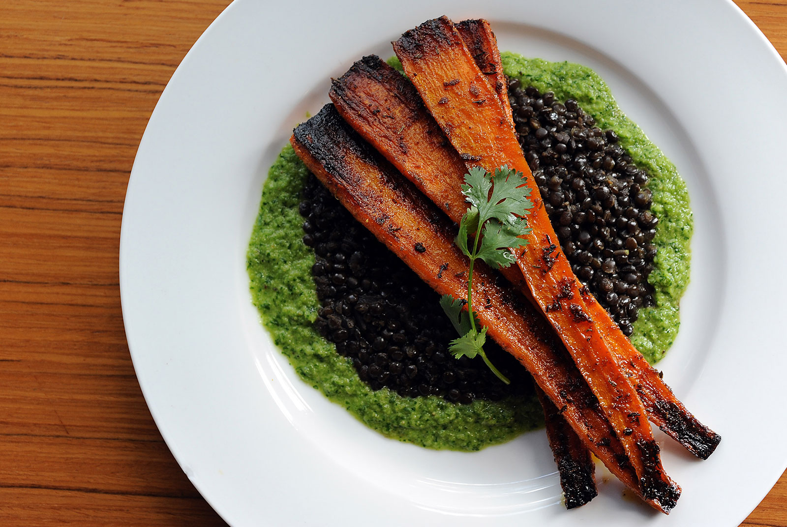Plate of roasted carrots atop black lentils and bright green harissa