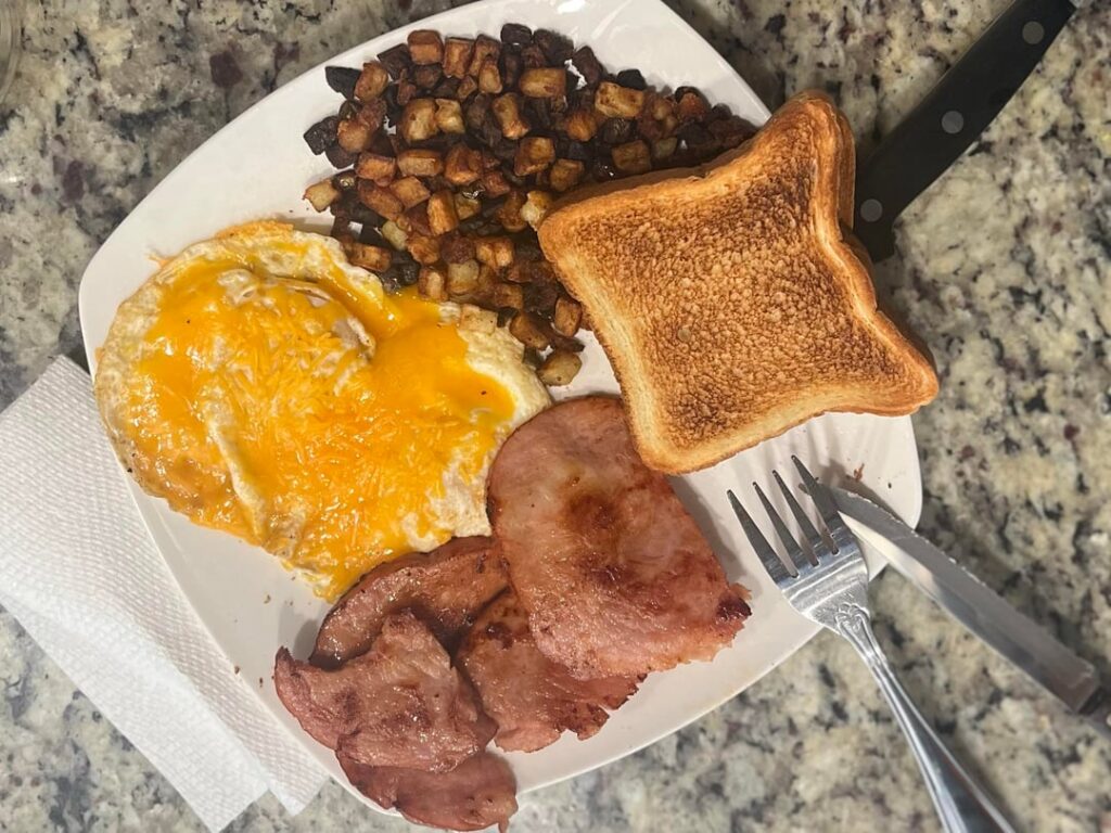 Over easy eggs with cheddar, home fries, ham steak and toast.