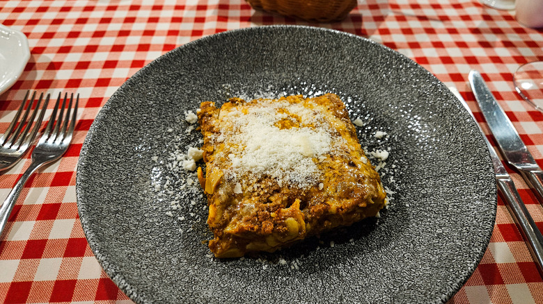 A hearty lasagna on a plate atop a red checkered tablecloth