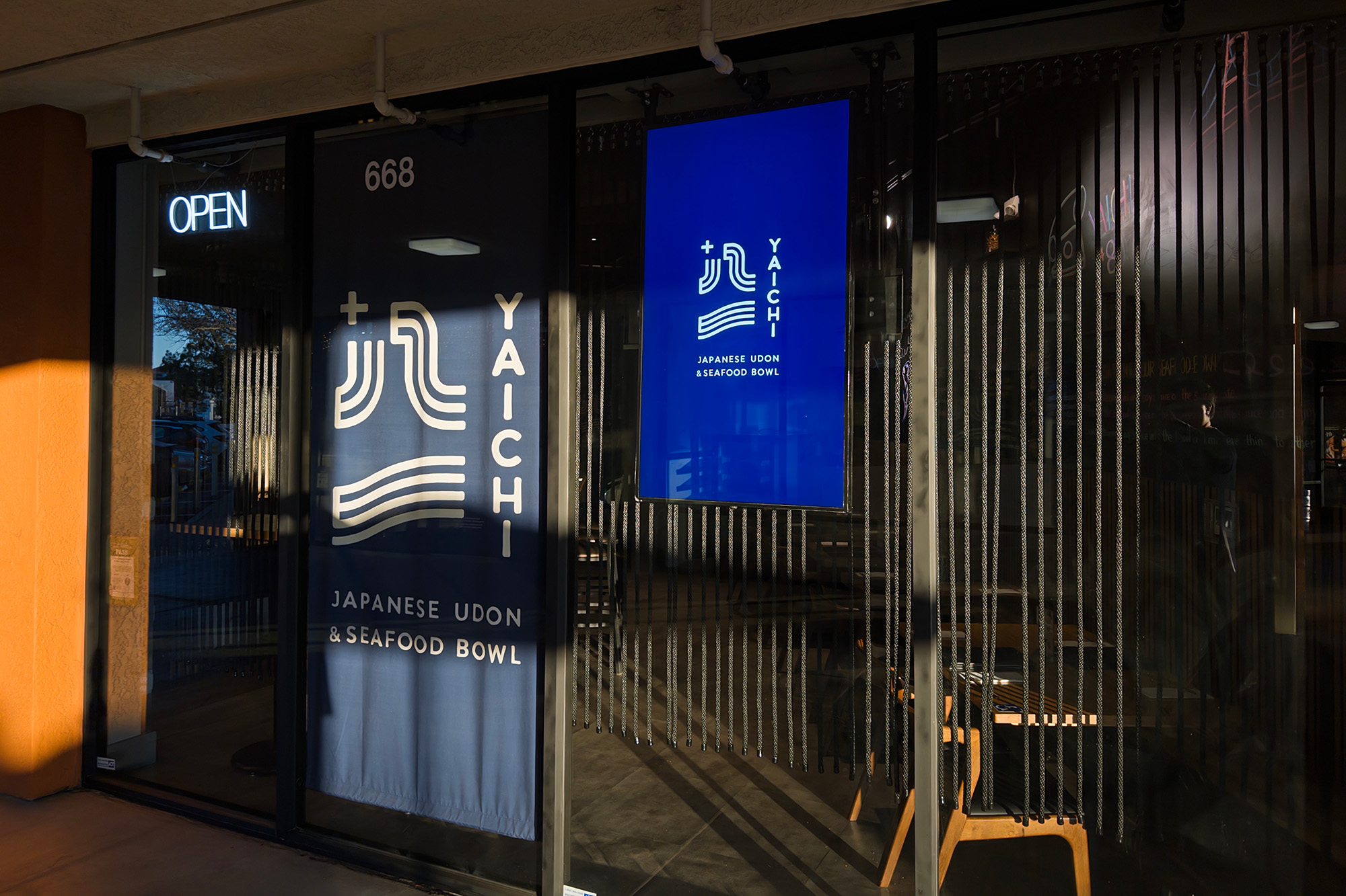 Exterior of a restaurant. The blue curtain hanging in the doorway reads, 