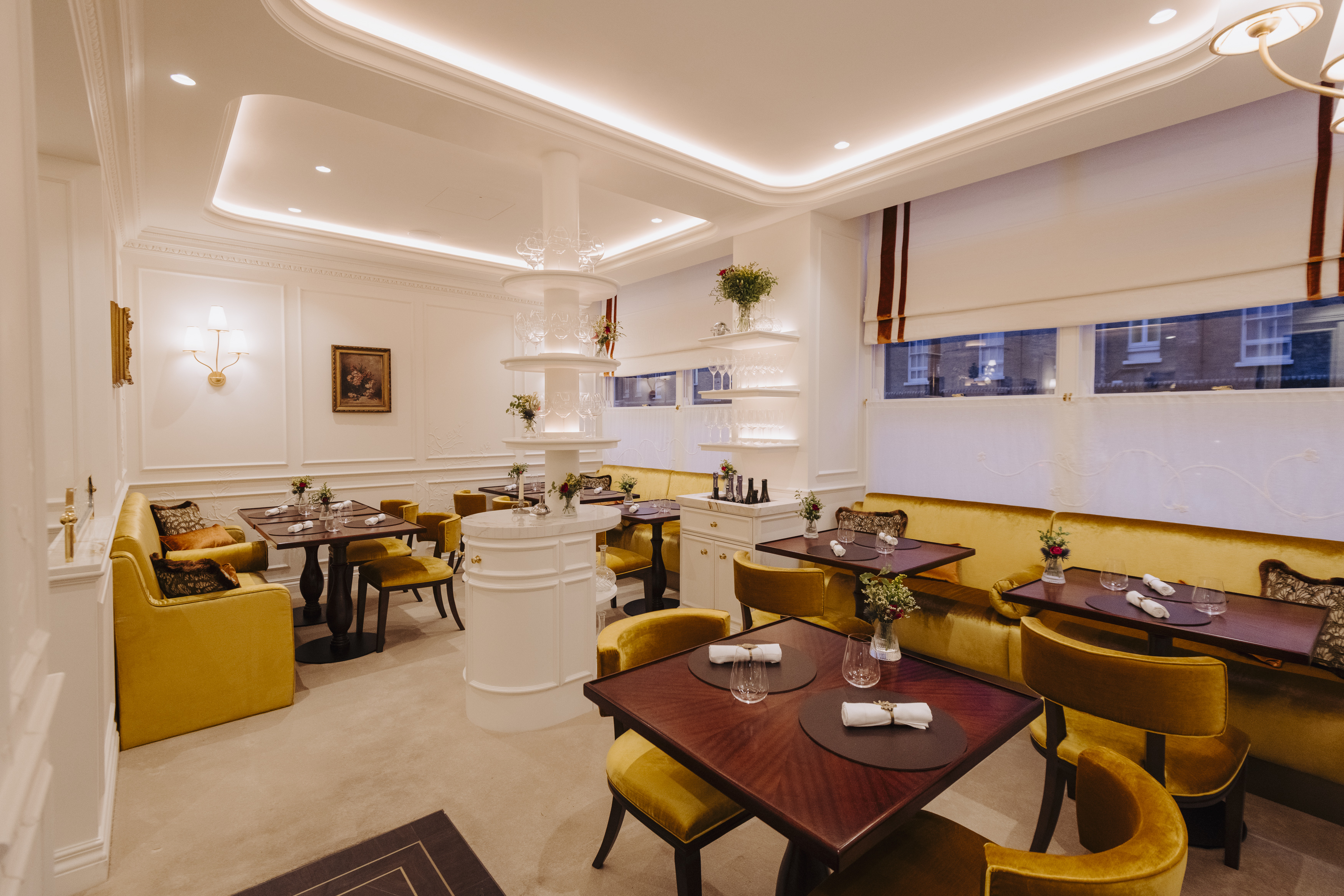 The dining room of Core restaurant with mustard yellow chairs and booths, wooden tables, and white walls with decorative molding.