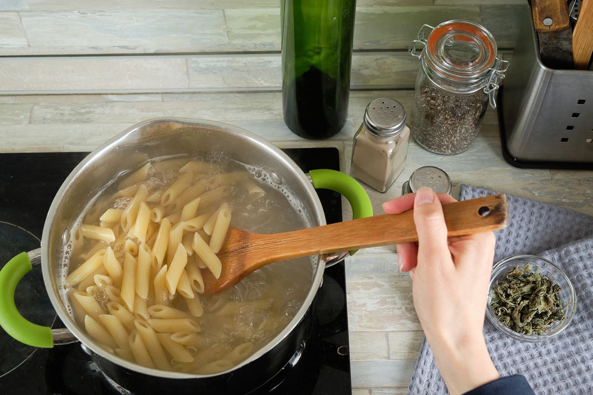 Cooking Italian pasta at home. A girl or a woman cooks and stirs Penne pasta in a saucepan. 