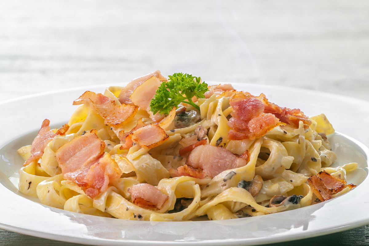 mushroom cream sauce spaghetti with bacon on white dish put on the wooded table in italian restaurant