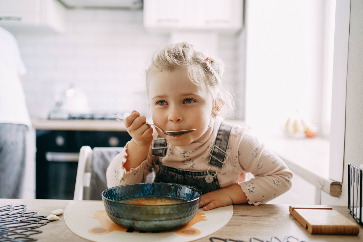 Little girl enjoying a healthy meal of soup in a domestic kitchen setting