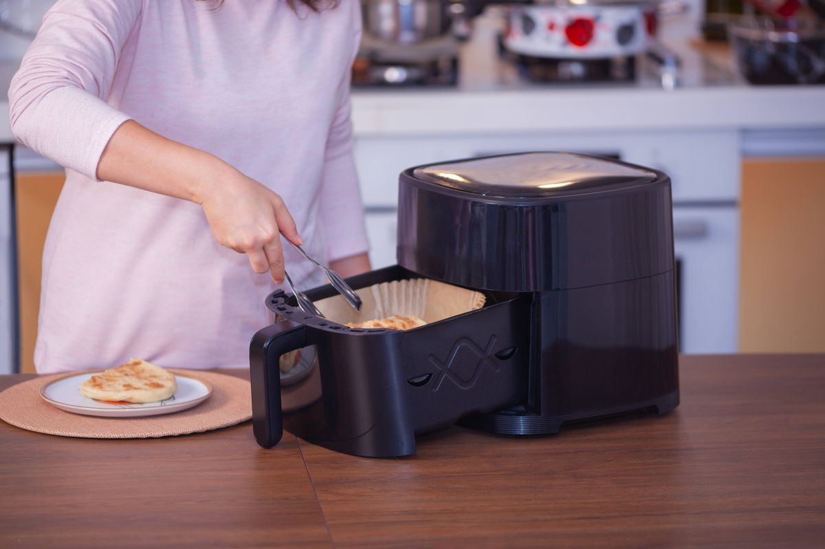 Woman using an air fryer to prepare food.