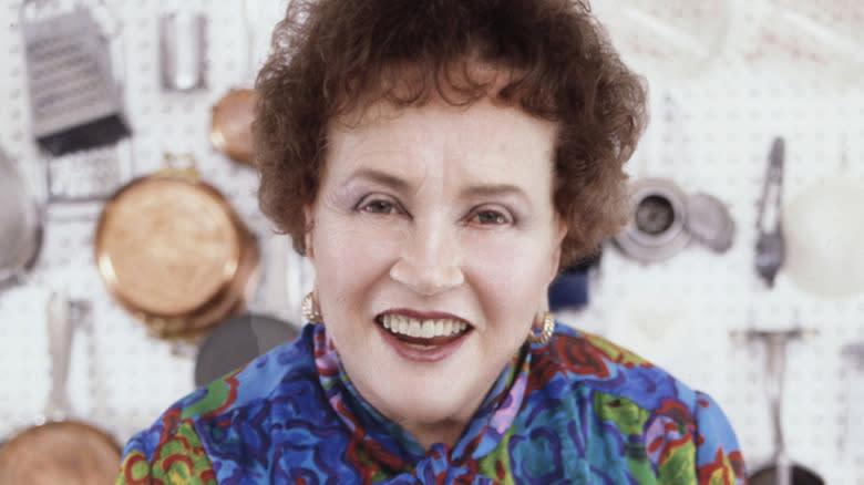 Julia Child smiling with pots and pans hanging on wall in background