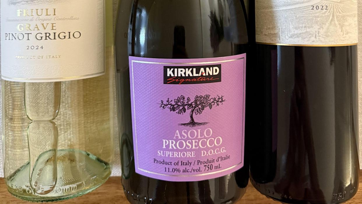 Three wine bottles: a 2024 Friuli Grave Pinot Grigio, a Kirkland Signature Asolo Prosecco with a purple label in the center, and a partially visible 2022 wine bottle on the right.