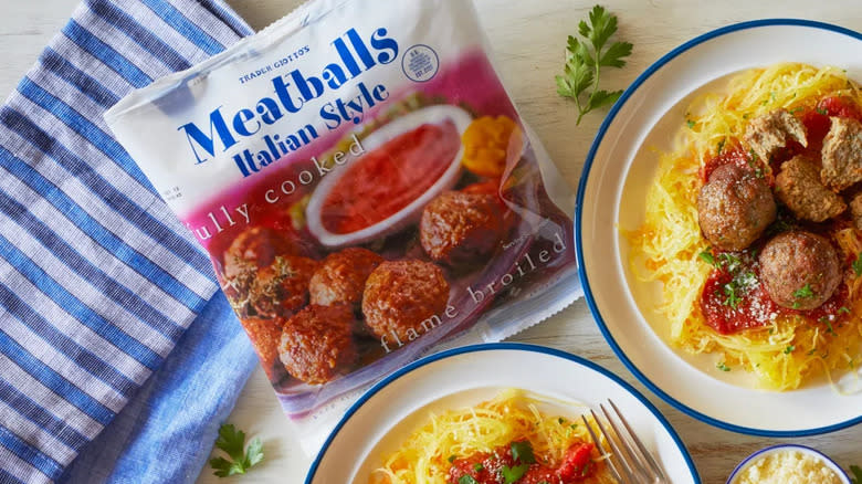 A bag of Trader Joe's Italian Style Meatballs alongside plates of spaghetti squash with meatballs