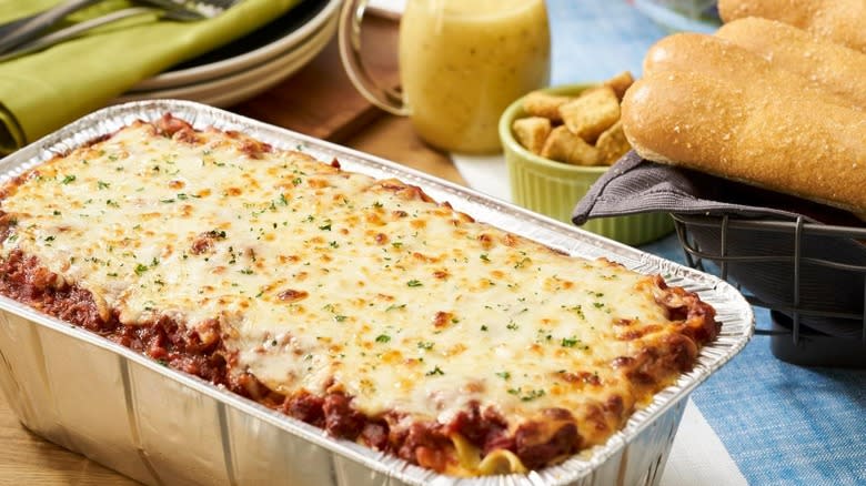 Silver foil family sized tray of lasagna from Olive Garden next to basket of breadsticks
