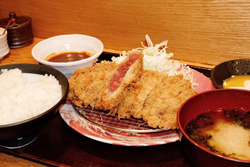 Sliced and fried wagyu cutlet at the center of a tray surrounded by rice, slaw, miso soup, soft egg and dipping sauce