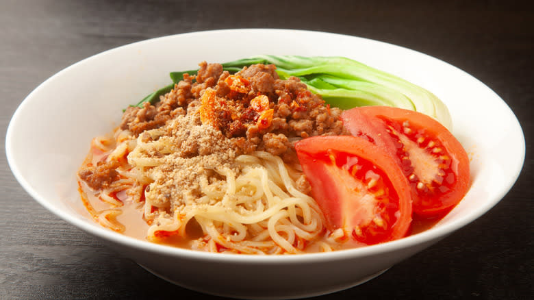 A bowl of ramen with tomato sauce, ground beef, green onions, and sliced tomatoes